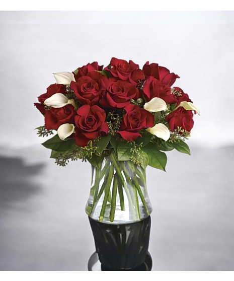 Red roses and white calla lilies in a clear glass vase with greenery